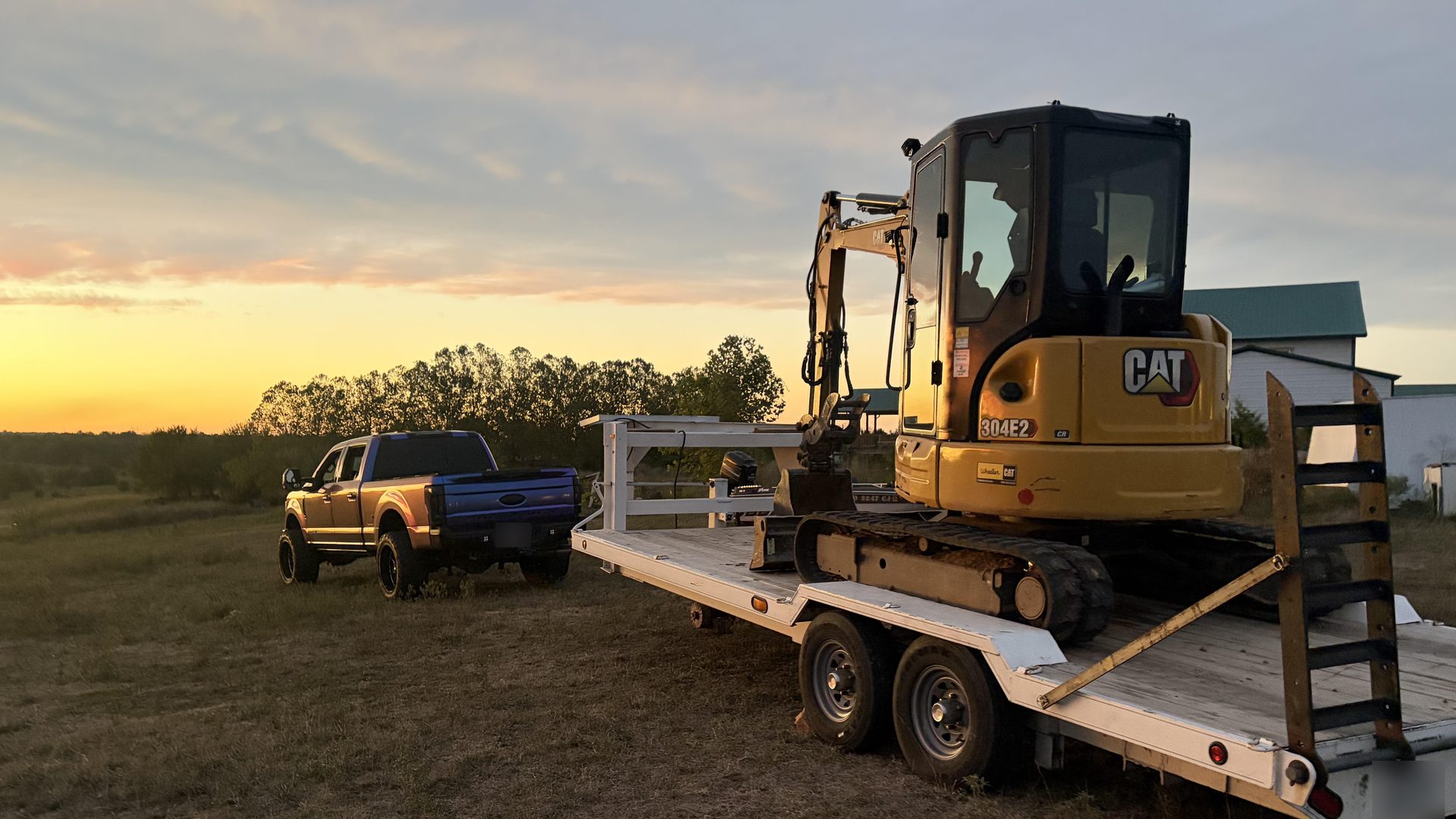 CAT mini excavator loaded on a trailer behind a pickup truck at sunset in the Springfield, MO area